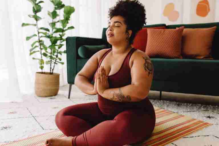 Women with eyes closed practicing yoga in living room. Sitting crossed legs with eyes closed and hands joined in prayer. Yoga for everybody