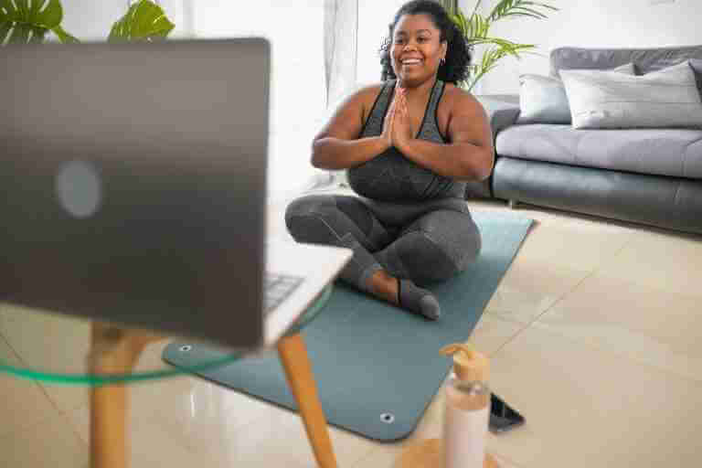 African young woman doing yoga virtual class with laptop at home