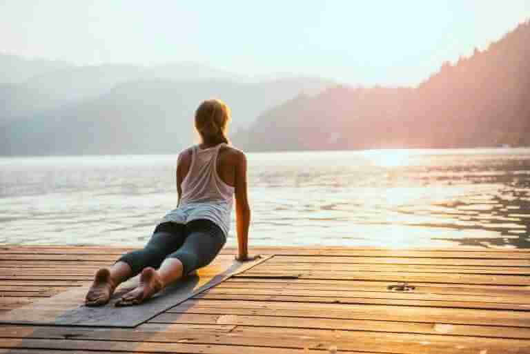 The benefits of a regular yoga practice. Women practicing yoga on a dock by a lake at sunrise.