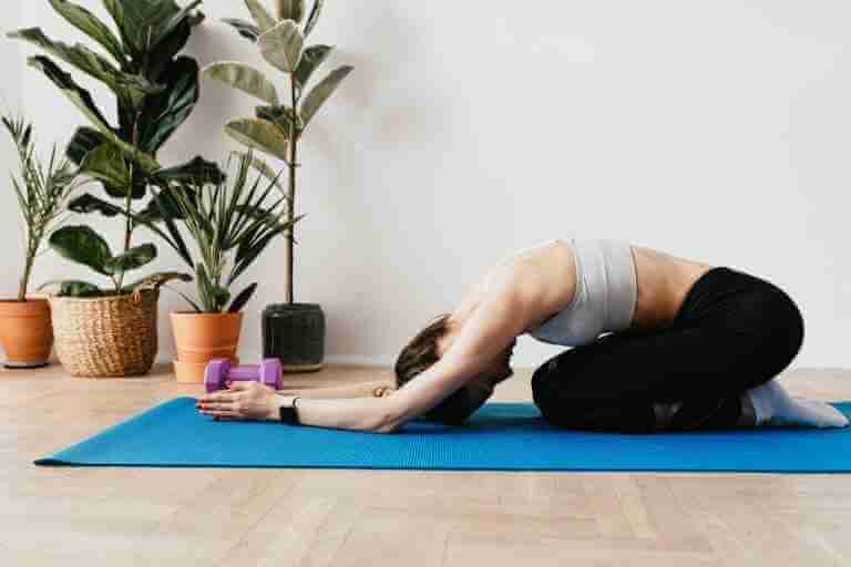 side view of a woman. she's bent over a yoga mat. doing child's pose. a good pose for yoga beginners