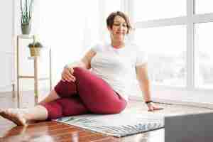 Yoga Helps Create a Calmer Mind. Here a plus size brunette woman practices yoga with body positivity with a laptop at home for livestream yoga.