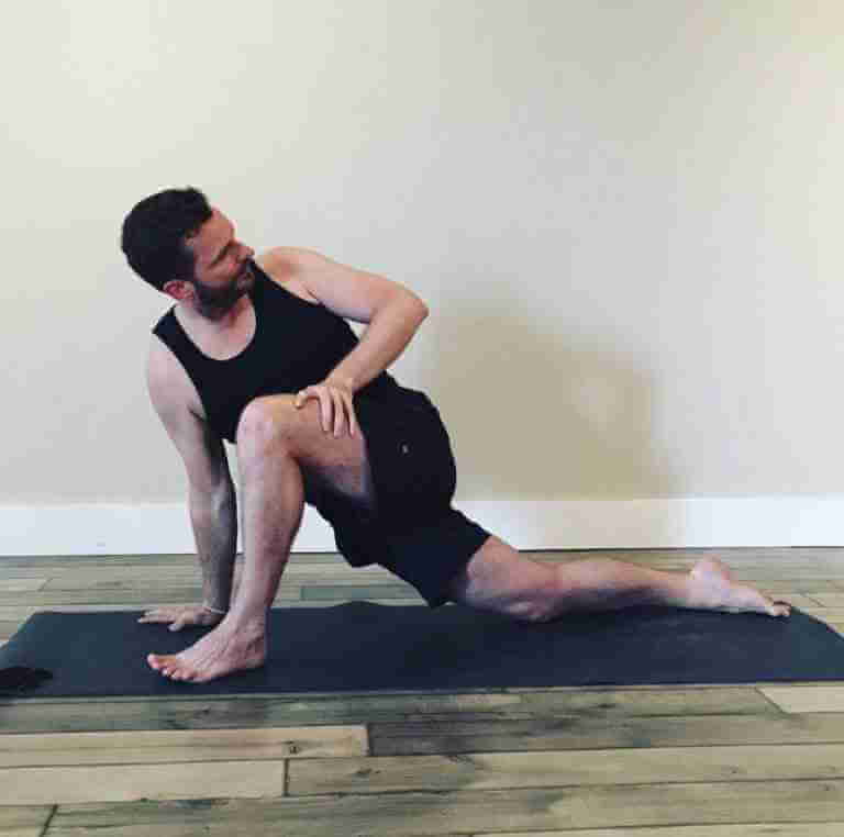 Man black top and shorts Performing Twisted Dragon Yoga Pose