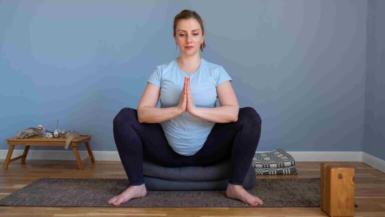 Pregnant woman practicing yogi squat pose Malasana sitting on yoga blocks and props. Using props to support her sacrum so she can do the pose and get the Yoga squat pose benefits