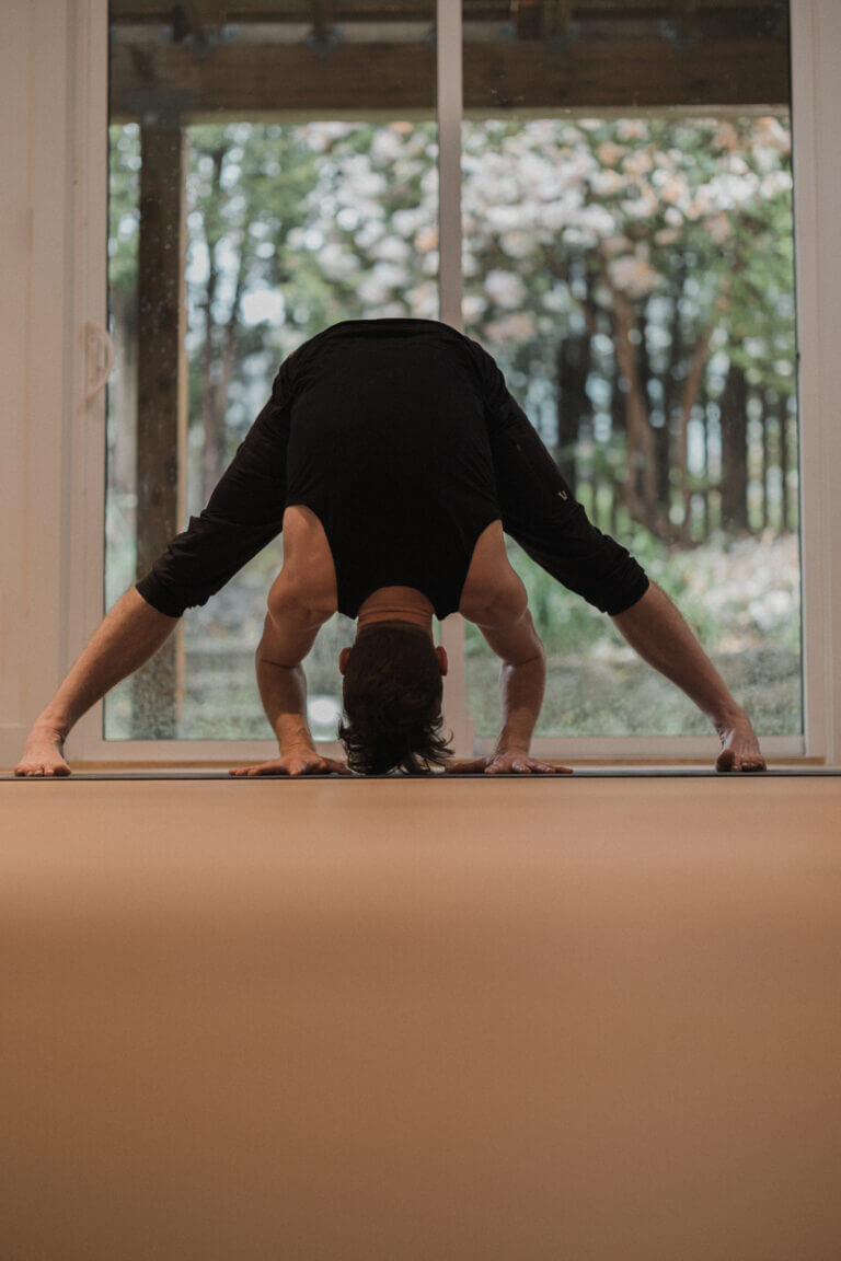 Man doing a wide legged forward fold for root chakra healing and red chakra meaning. focused on Muladhara, Kevin Parenteau Ashtanga Yoga Teacher