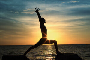 Silhouette of perfect body man act yoga on the rock with sea sunset background. inspired by yoga quote