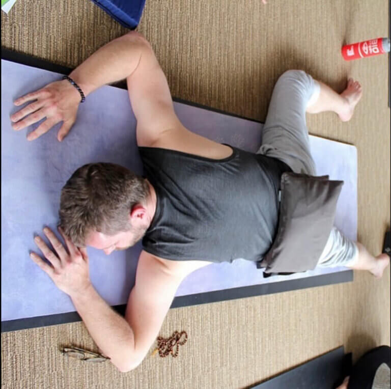 man lying on front with a sand bag on back. counter to Caterpillar yin yoga Pose benefits Paschimottanasana
