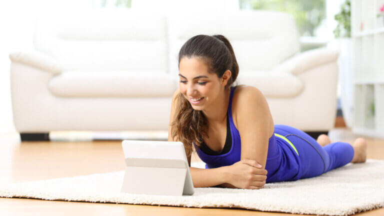 picture of woman doing a sphinx yoga pose while watching a tablet