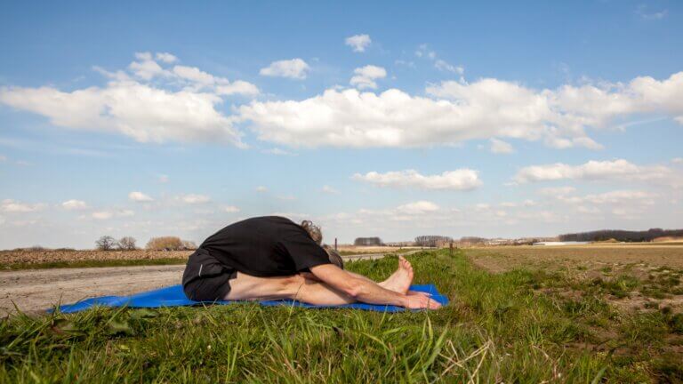 man doing a caterpillar yoga pose outside in the grass. YACEP ayurveda training