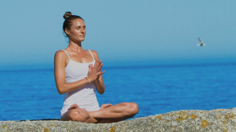 Melanie de Villiers sitting crossed leg doing yin yoga on a beach
