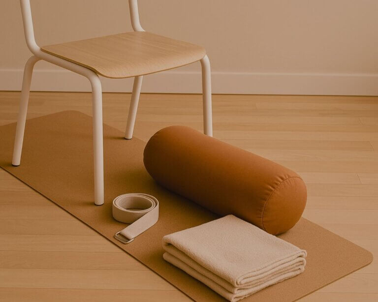 Yoga setup with chair, strap, bolster, and folded blanket neatly arranged on a mat in soft daylight.