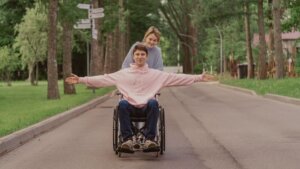 Wheelchair or chair-based yoga student lifting arms overhead outside with natural light.