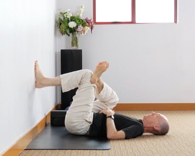 Bernie Clark practicing a gentle figure four pose on a mat indoors