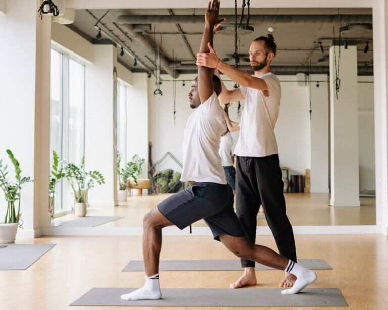 Yoga teacher assisting a student while practicing on a mat.