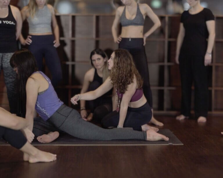 Christina Raskin Yoga Teacher addressing class on knees, soft facial expression, gesturing gently while students listen.