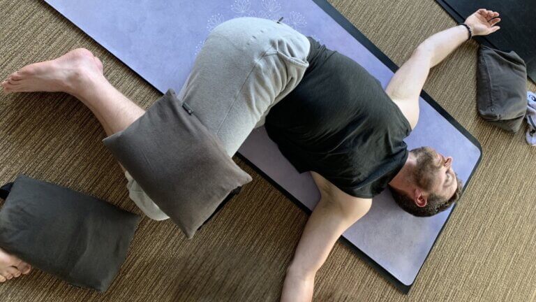 Kevin Parenteau doing a reclining twist pose with sandbag yoga props