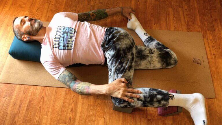 Risto Duggan demonstrating cat pulling its tail with bolster and block yoga props