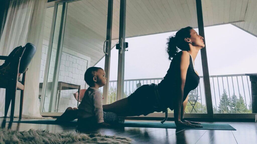 Laura Roman practicing Upward-Facing Dog at home with a baby nearby.