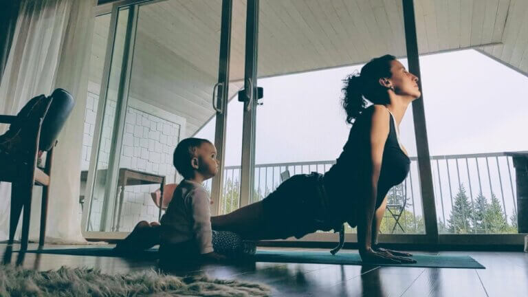 Laura Roman practicing Upward-Facing Dog at home with a baby nearby.