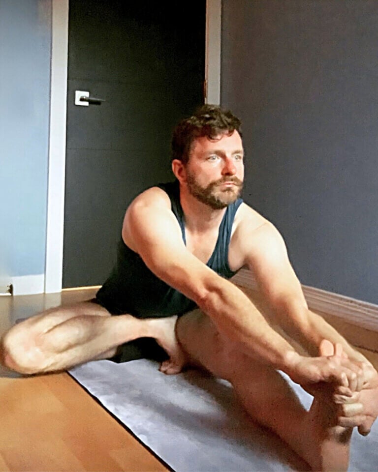 Kevin holding his extended foot in Janu Sirsasana C, with the other heel raised.