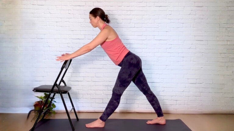 Christina Raskin in Pyramid Pose with one foot forward and both hands on a chair backrest.